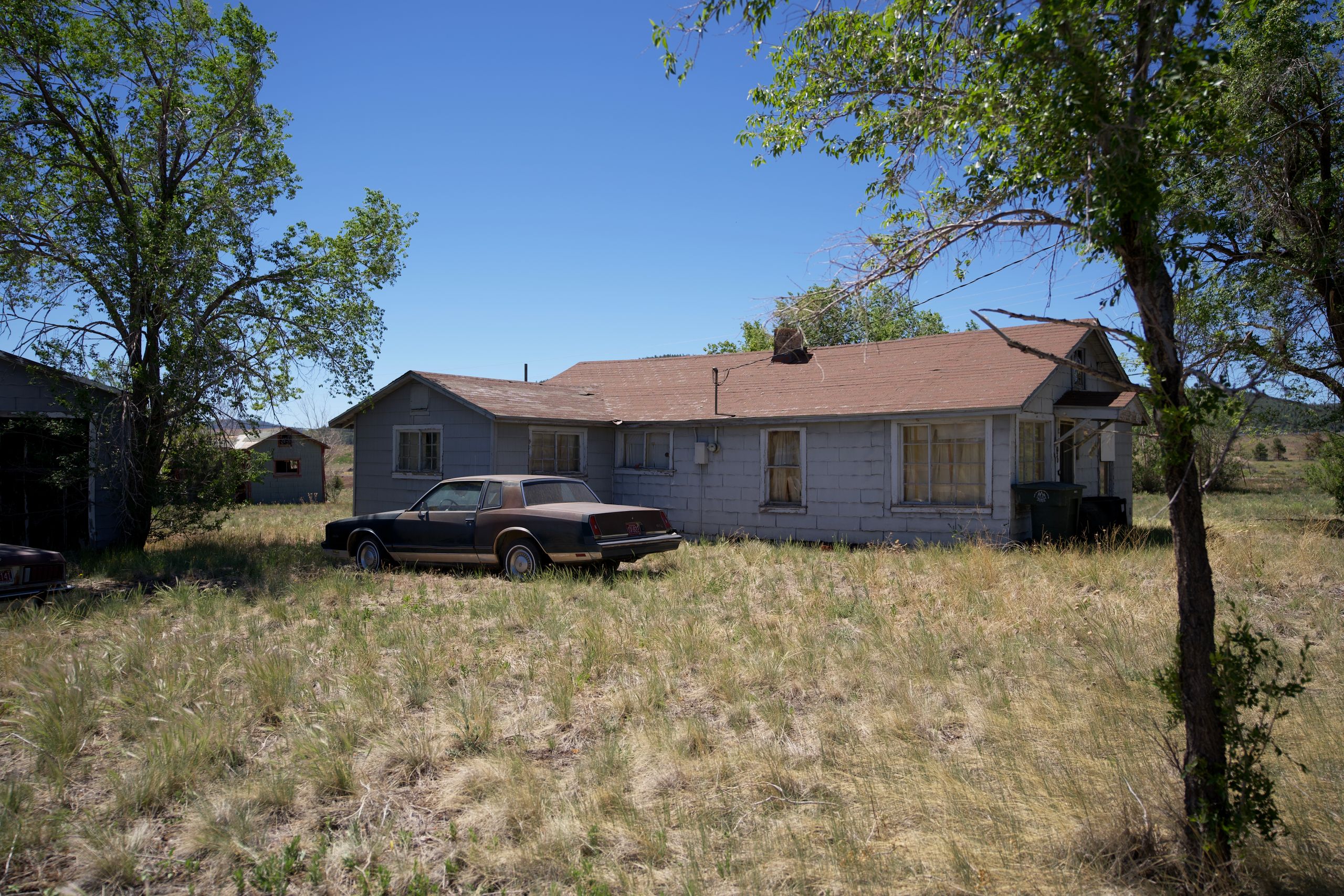 An old, abandoned house with a vintage car in an overgrown yard, situated outdoors.
