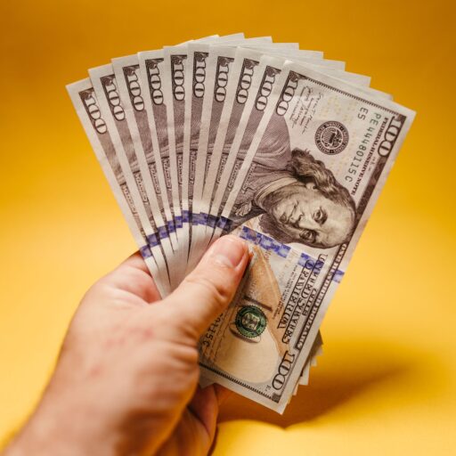 Close-up of a hand displaying US dollar bills against a bright yellow backdrop, signifying wealth and finance.
