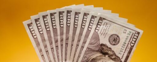 Close-up of a hand displaying US dollar bills against a bright yellow backdrop, signifying wealth and finance.